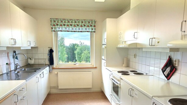 Eine Küche mit weißen Schränken, einem Herd, einem Backofen, einer Spüle und einem Fenster mit Blick auf Bäume.