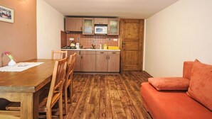 A compact kitchen with wooden cabinets, a microwave, and a sink. There is a wooden dining table with chairs and a red sofa. - Lovely apartment in villa for 4 guests with pool, WIFI, TV and pets allowed (Prachatice)