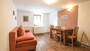 A cozy living area with a sofa, wooden dining table, and chairs. A window provides natural light, and a radiator is visible on the wall. - Lovely apartment in villa for 4 guests with pool, WIFI, TV and pets allowed (Prachatice)