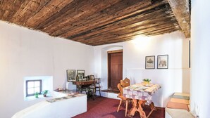 A rustic room with a wooden ceiling, a small window, a wooden table with chairs, and a door.