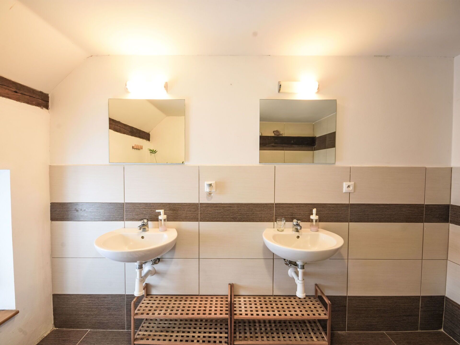 A bathroom with two sinks, a wooden shelf, and a mirror above each sink.