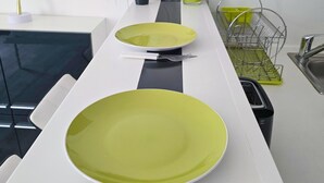 Una encimera de cocina con dos platos verdes, un cuchillo y un tenedor. Hay una planta verde en una maceta y un escurreplatos verde.