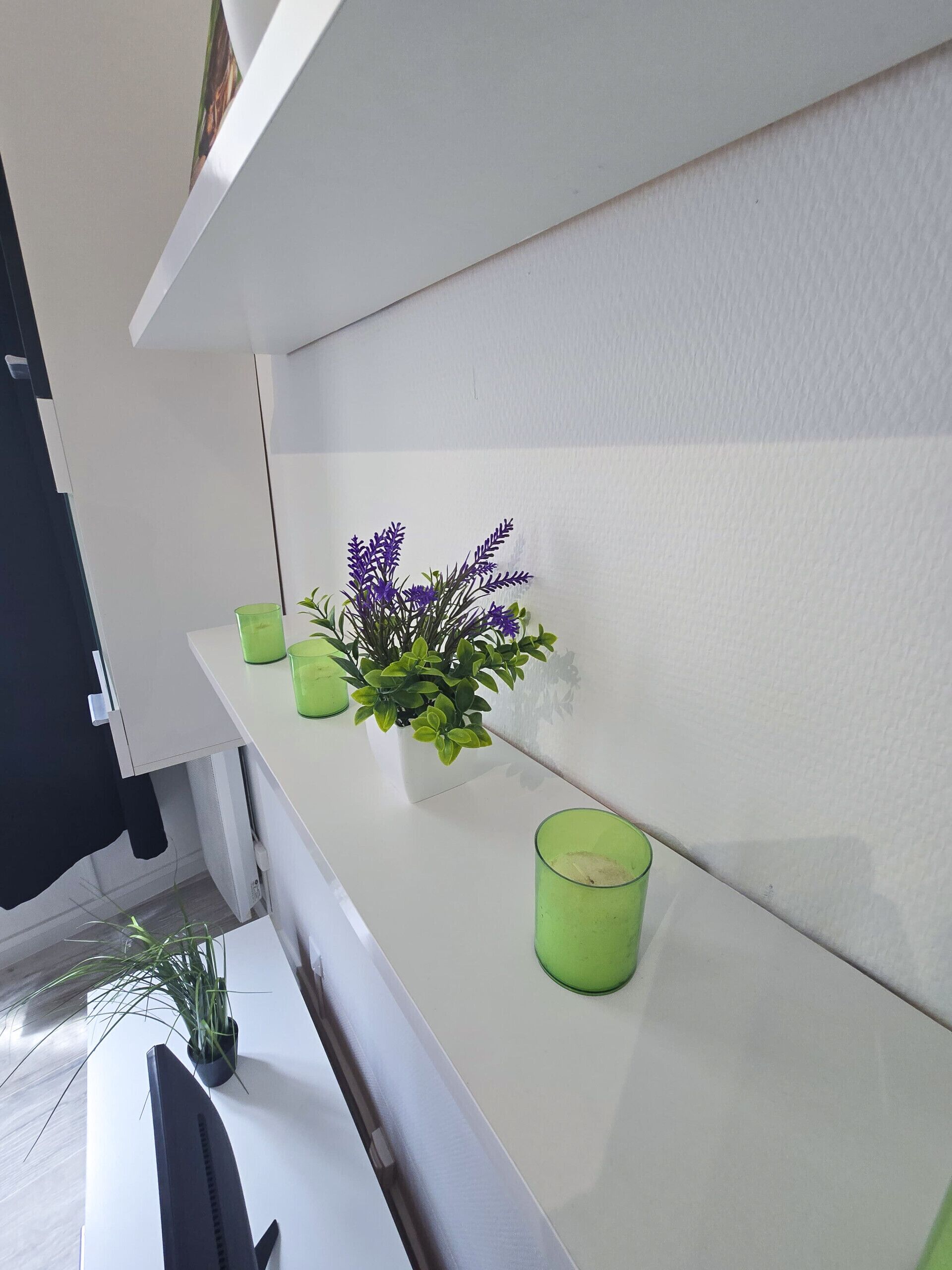 A white shelf with a potted plant and two green glasses.