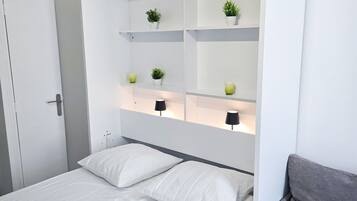 Een moderne slaapkamer met een bed, een grijze bank en ingebouwde kasten met planten en lampen.