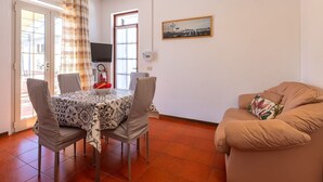 A dining area with a table set for two, a sofa, and a television on the wall. - Beautiful apartment for 2 guests with WIFI, A/C, TV, terrace and pets allowed (Olbia)