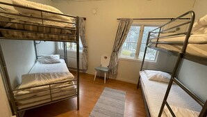 Um quarto de dormitório com beliches, uma mesa pequena e uma janela com cortinas.