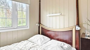 A bedroom with a wooden headboard, a window with blinds, a bedside table with a lamp, and a floral-patterned bedspread. - 6 Person Holiday Park Home in Otterup (Otterup)