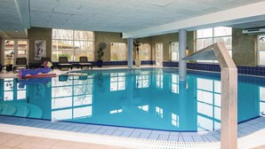 Ein Hallenbad mit klarem, blauen Wasser, gefliesten Wänden und einigen Liegestühlen.