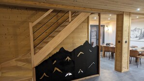 A wooden staircase leading to a dining area with a black wall featuring mountain silhouettes. - Modern chalet La Tanière with sauna in Le Chinaillon (Le Grand-Bornand)