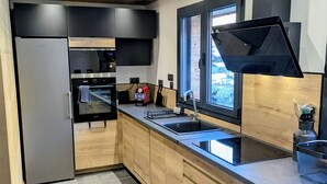 Moderni keittiö, jossa on puukehikoiset kaapit, ruostumattomasta teräksestä valmistettu jääkaappi, sisäänrakennettu uuni ja musta liesituuletin.