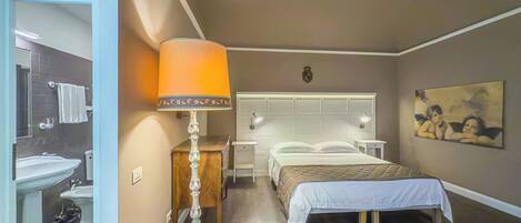 Une chambre à coucher comprenant un lit, des tables de chevet, une lampe, un tableau, et une salle de bain avec un lavabo et un miroir.