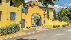 A yellow building with a large arched entrance, a sign for Villa Le Farnete, and a parking sign. - B&B Villa Le Farnete (Comeana)