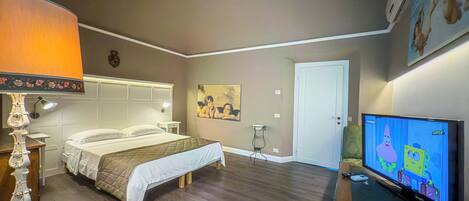 A hotel room with a bed, a nightstand, a lamp, a painting on the wall, a door, and a television displaying an animated show.