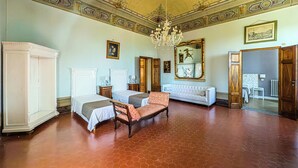 A room with two beds, a sofa, a chandelier, and a large mirror. - B&B Villa Le Farnete (Comeana)