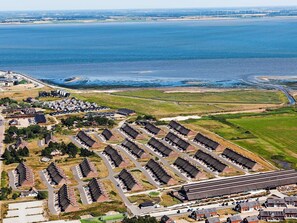 An aerial view of a coastal area with a row of uniform houses, a marina, and a distant wind farm.