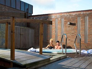A couple relaxing in a hot tub with a wooden pergola overhead.