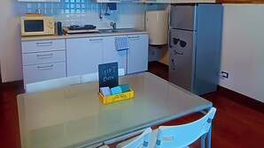 Et kompakt køkken med hvide skabe, en mikroovn, et køleskab og et lille bord med to stole. Der står et skilt på bordet med teksten 'GIFT BOX'.