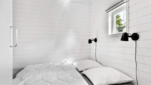 A small, single-bed room with white walls and a sloped ceiling. There is a window with a view of greenery outside. Two black desk lamps are mounted on the wall. - 6 Person Holiday Park Home in Malling (Malling)