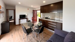 A modern kitchen with dark cabinets, a granite countertop, and a built-in sink. There is a dining area with a glass table and black chairs.