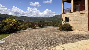 Un edificio de piedra con balcón, un camino de adoquines y un paisaje montañoso al fondo.