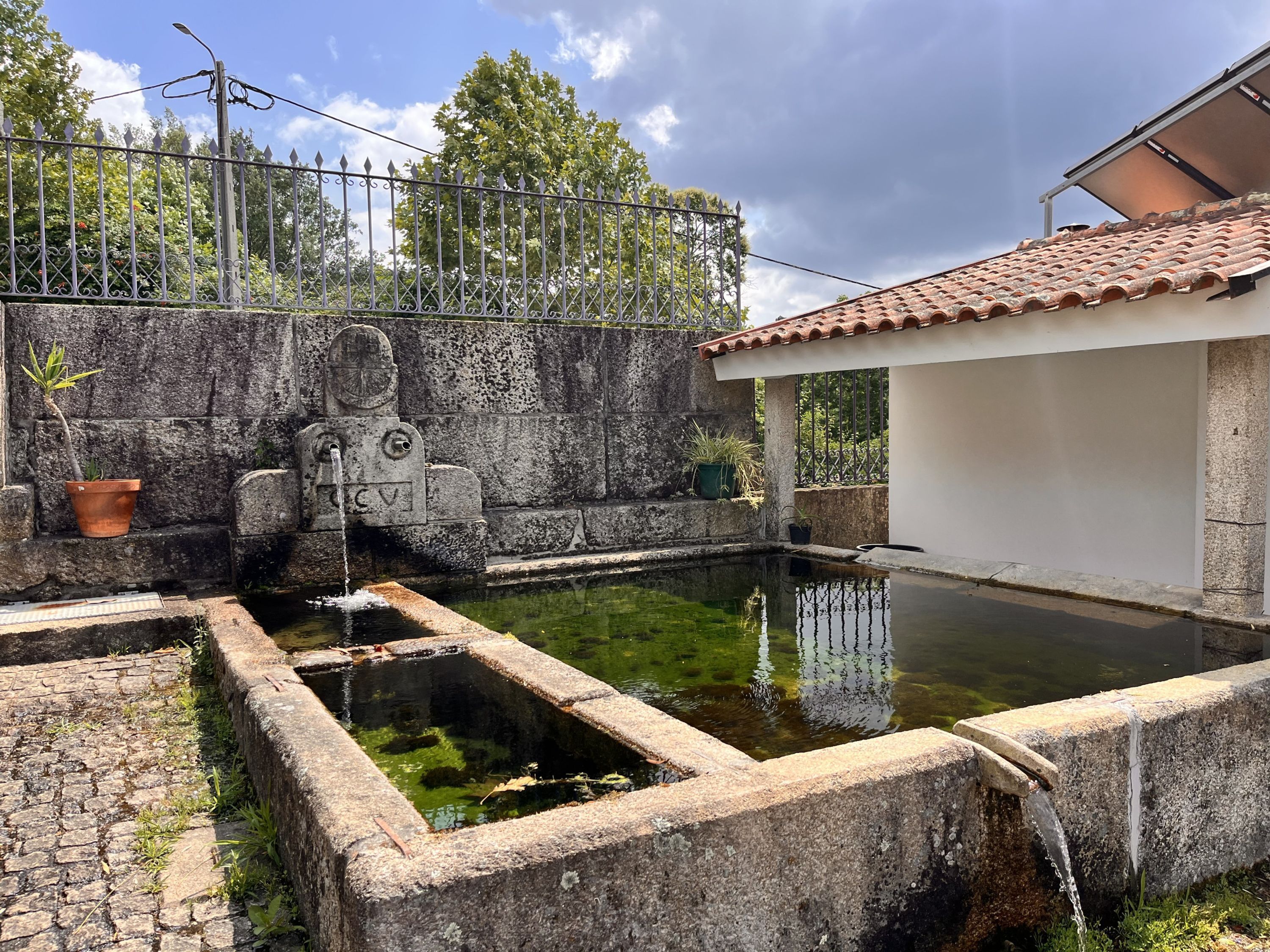 Un patio con una fuente, muros de piedra y techo de tejas.