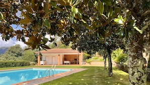 A pool with a tiled deck, a covered outdoor seating area, and a view of the surrounding landscape.
