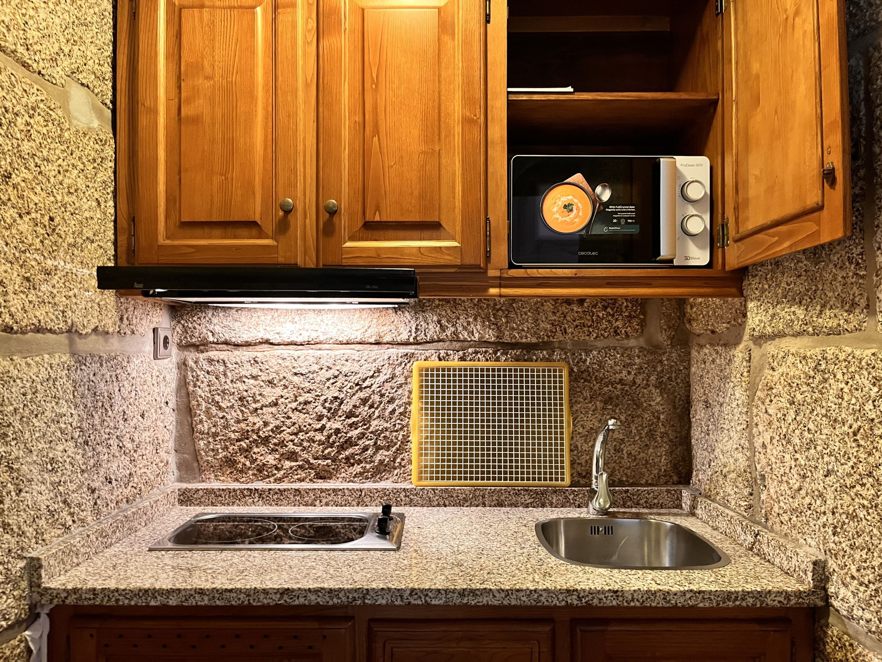 A kitchen with granite countertops, a stainless steel sink, wooden cabinets, a microwave, and a built-in range hood.