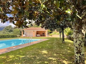 A pool area with a tiled deck, a covered seating area, and a view of a mountainous landscape.