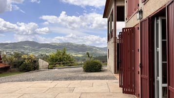 Ein Gebäude mit einer steinernen Fassade und roten Fensterläden, einem gepflasterten Innenhof und Blick auf ferne Hügel.
