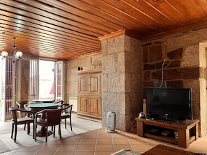 A room with a wooden ceiling, stone walls, a billiards table, and a television on a wooden stand.