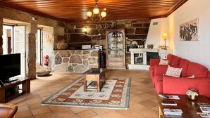 A cozy living room with a stone fireplace, wooden ceiling, and a red sofa. - Nomad s Country - Cimo de Vila The Poolside Haven (Cabeceiras de Basto)