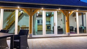 Ett takförsett utomhusområde med ett matbord och stolar, en trappa som leder upp till en övre våning och utsikt in i byggnadens interiör.