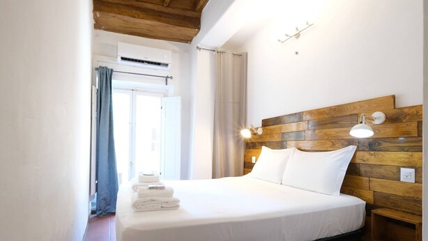 Ein Hotelzimmer mit einem hölzernen Kopfteil, einem Bett mit weißer Bettwäsche, einem Nachttisch und einer Wandleuchte.