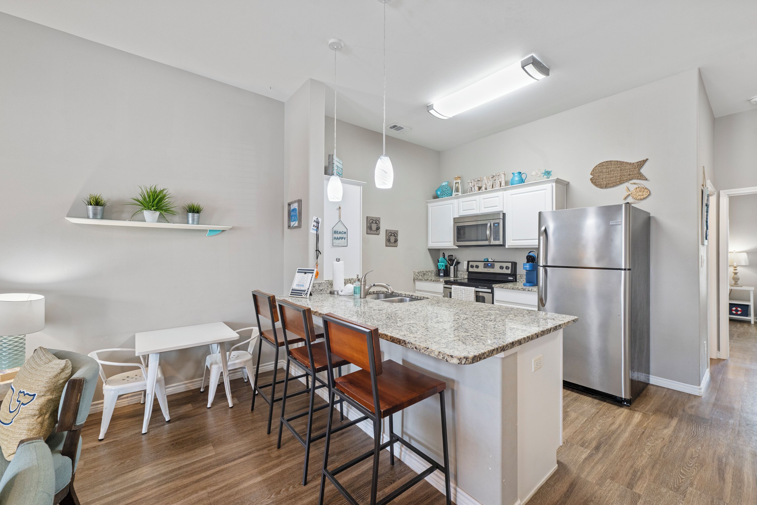 Une cuisine moderne dotée d’un îlot central, de meubles blancs, d’appareils électroménagers en acier inoxydable et d’un coin repas avec des tabourets de bar.