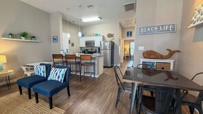 A modern kitchen with a central island, a dining area with a glass table, and a living room with a blue sofa.