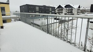 Un balcón cubierto de nieve con barandilla metálica que da a una hilera de edificios de varios pisos.