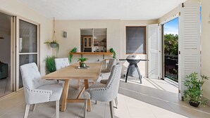 A dining area with a wooden table and four upholstered chairs, a ceiling fan, and a grill outside. - Lakeside Luxe Retreat - Pool View BBQ Spa Bath (Cairns)