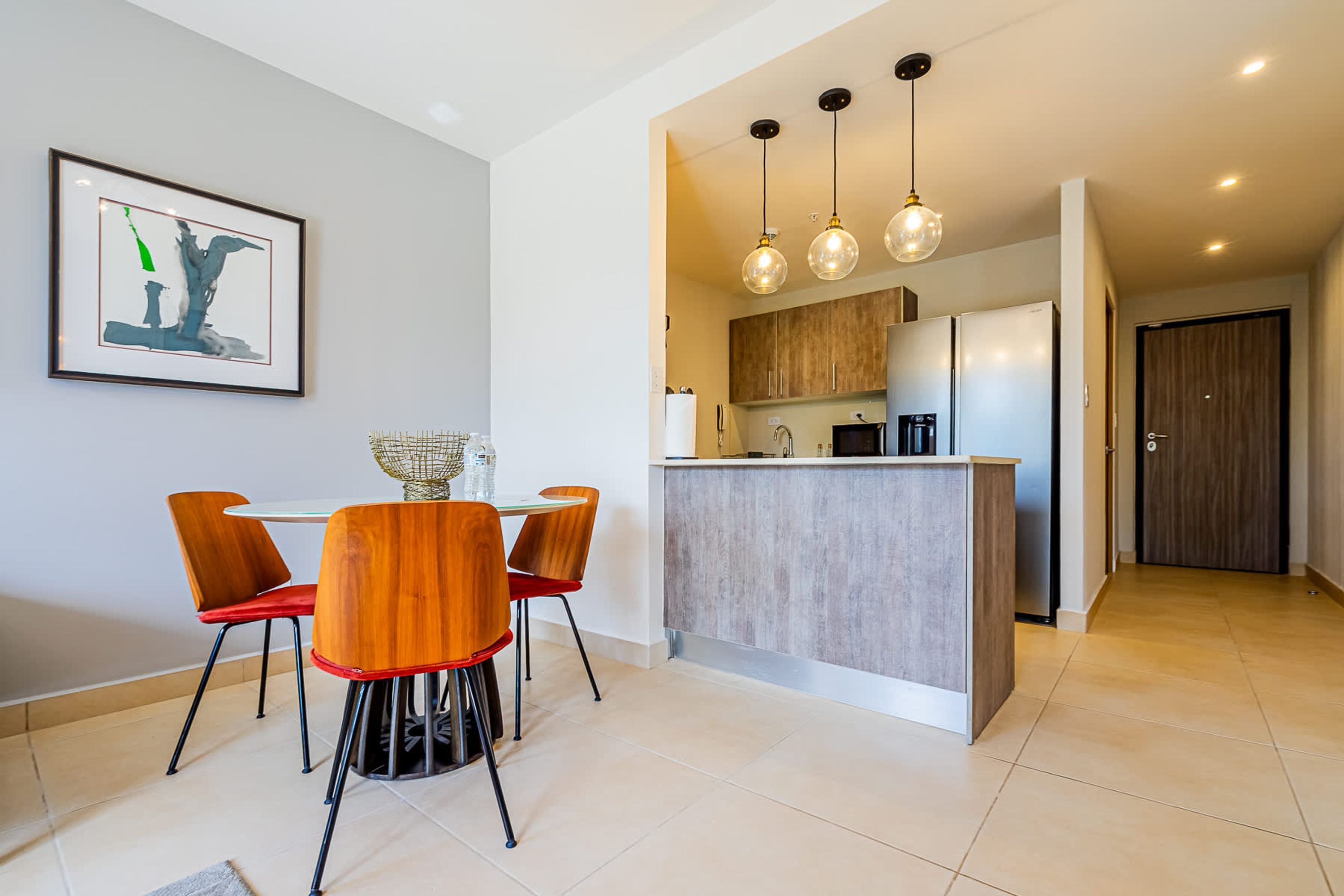 A modern kitchen with a central island, pendant lights, and a dining area with a table and chairs.