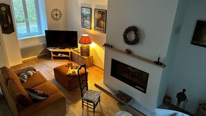 A living room with a sofa, a chair, a TV, a fireplace, and a window with blinds. - Cottage by River With Spa Near Carcassonne (Caudebronde)