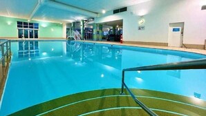 An indoor swimming pool with clear water, a diving board, and a lifeguard chair.