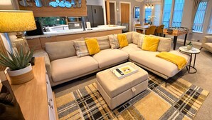 A modern living room with a beige sectional sofa, a coffee table, and a dining area with a table and chairs.
