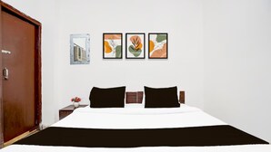 A hotel room with a large bed, two black pillows, a white duvet, and three framed artworks on the wall. - Hotel R K Palace Agra (Agra)