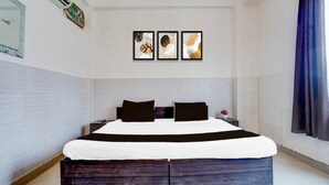 A bedroom with a bed, a nightstand, a wall-mounted picture, and a window with curtains. - Hotel R K Palace Agra (Agra)