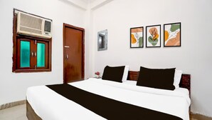A hotel room with a large bed, a window with curtains, an air conditioning unit, and three framed artworks on the wall. - Hotel R K Palace Agra (Agra)