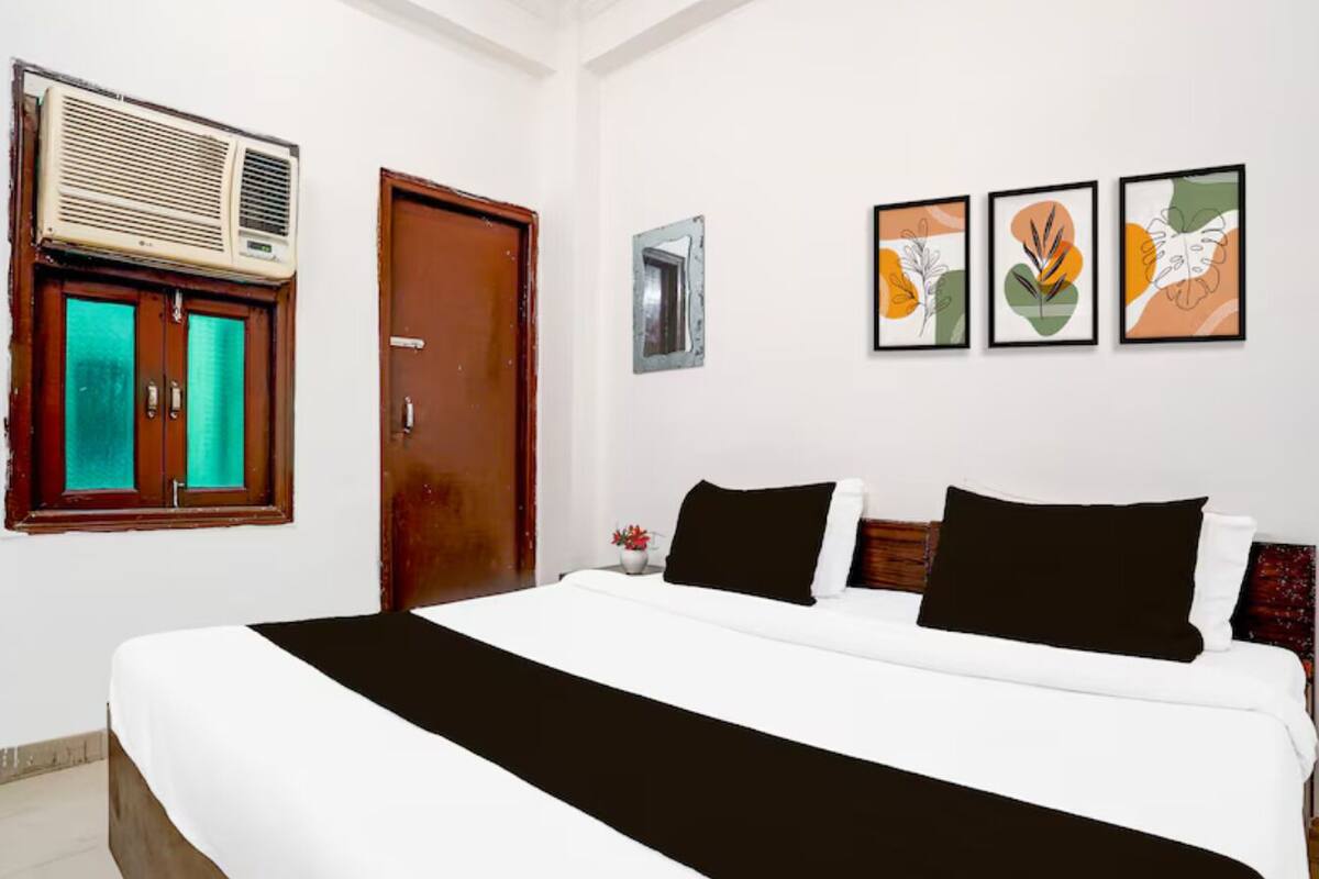 Une chambre d’hôtel avec un grand lit, une fen être avec des rideaux, un appareil de climatisation et trois œuvres d’art encadrées accrochées au mur.