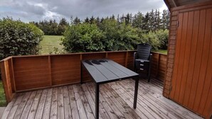 Une terrasse en bois avec une table et des chaises, entourée d’une clôture en bois et d’une végétation luxuriante.
