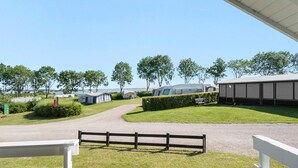 Un terrain de camping avec des emplacements pour camping-cars et des tentes, un chemin de gravier et une zone délimitée par une clôture.
