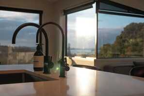 A kitchen with a modern faucet, a bottle of wine, and a view of the outdoors through large windows. - Elegant Urban Retreat in Freemans Bay. (Auckland)