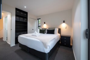 A modern bedroom with a large bed, built-in storage, and bedside lamps.
