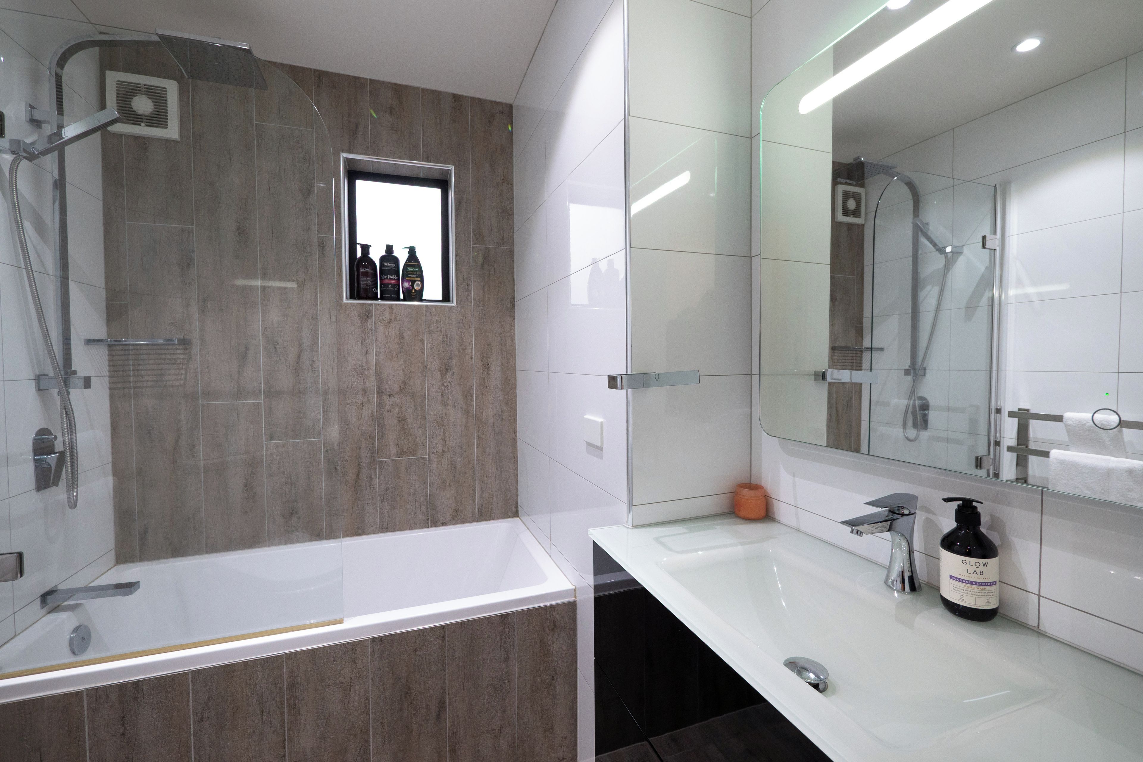 A modern bathroom with a bathtub, shower, and a large mirror.